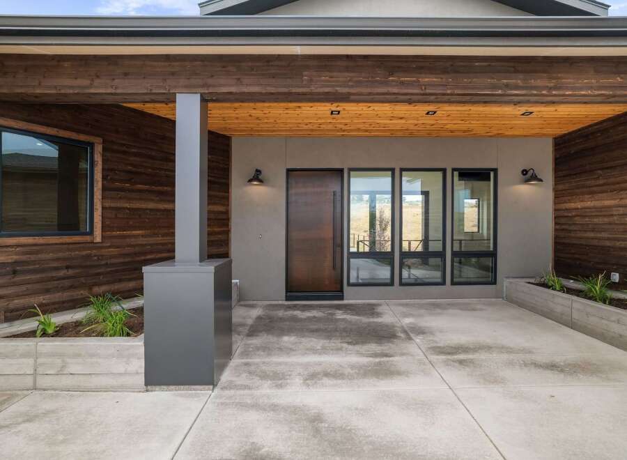 Experience modern living with this stunning home featuring a sleek wood-paneled exterior and a welcoming covered entryway.
