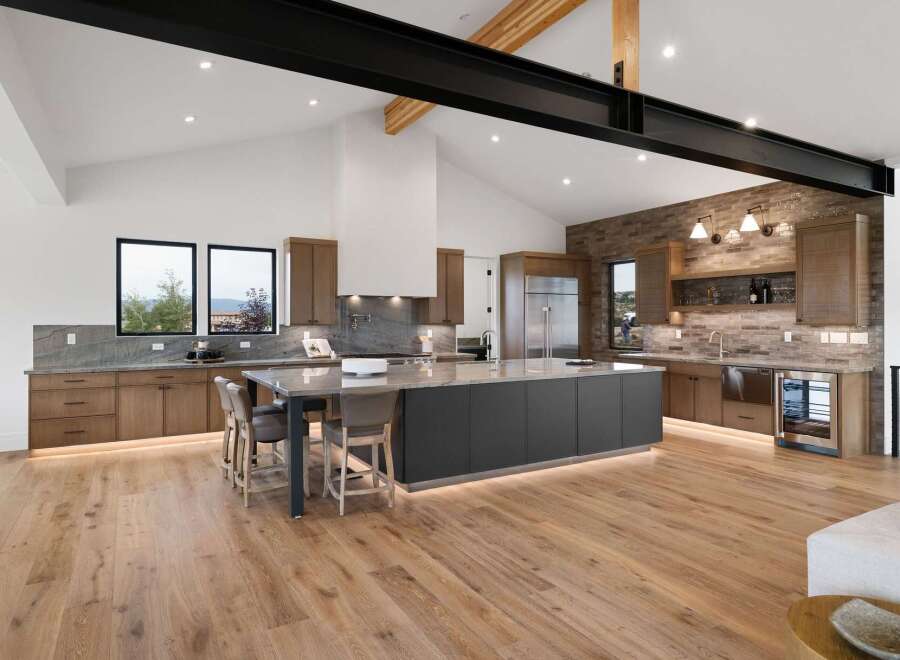 Experience luxury modern living in this stunning kitchen featuring a large island with seating, sleek cabinetry, and a dramatic vaulted ceiling with exposed beams.