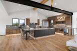 Experience luxury modern living in this stunning kitchen featuring a large island with seating, sleek cabinetry, and a dramatic vaulted ceiling with exposed beams.