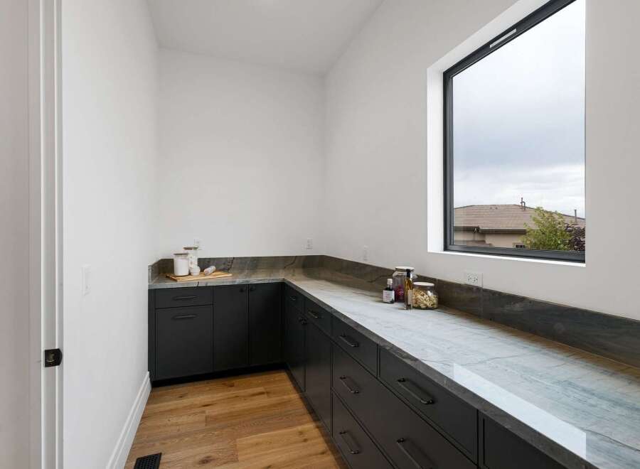 Discover this modern pantry featuring sleek dark cabinetry and a stunning marble countertop.