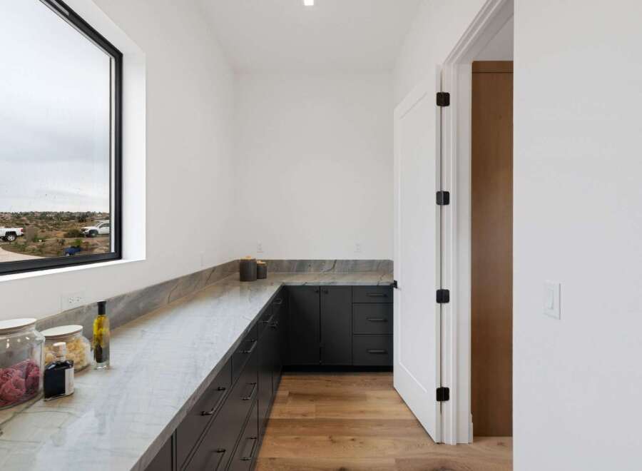 Discover modern functionality in this spacious pantry, featuring sleek dark cabinetry and elegant marble countertops.