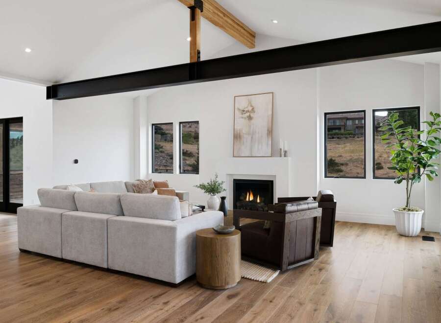 Experience modern living in this stunning great room, featuring a vaulted ceiling with exposed black steel beams and a cozy gas fireplace.