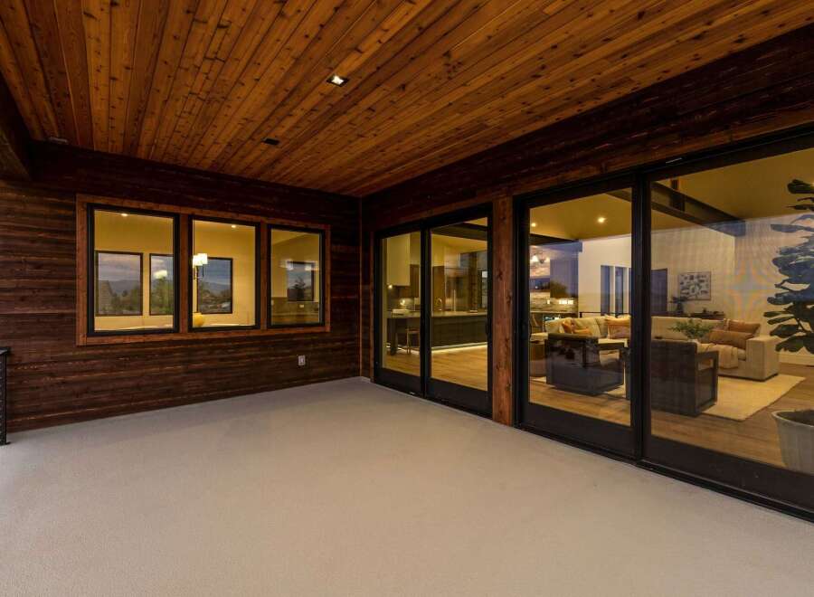Experience seamless indoor-outdoor living with this stunning covered patio, featuring a warm wooden ceiling and expansive glass doors that open into a beautifully appointed living space.