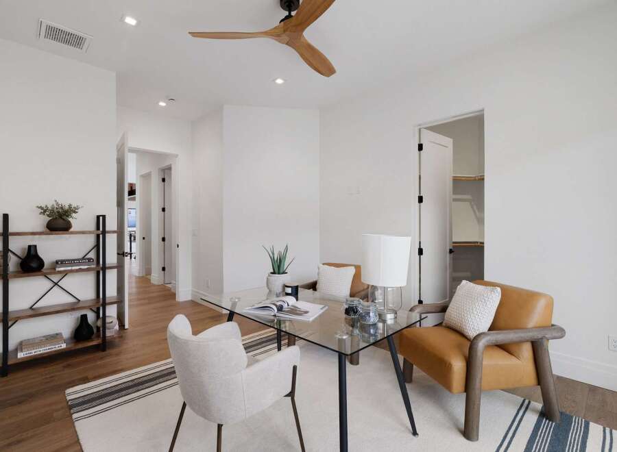 This modern home office features a sleek glass-top desk with a white armchair and a stylish tan leather accent chair, perfect for productive work sessions.
