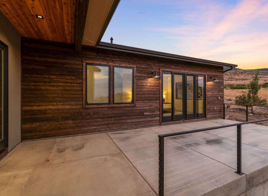 Experience modern living with this stunning home featuring a sleek wooden exterior and expansive concrete patio.