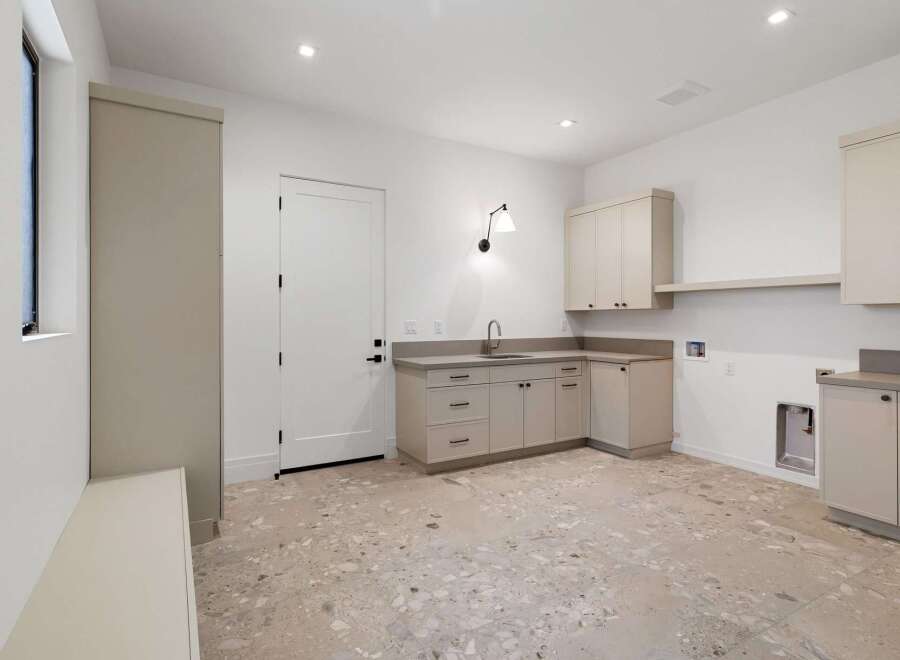 Discover this spacious laundry room featuring a convenient utility sink and ample cabinet storage for all your organizational needs.