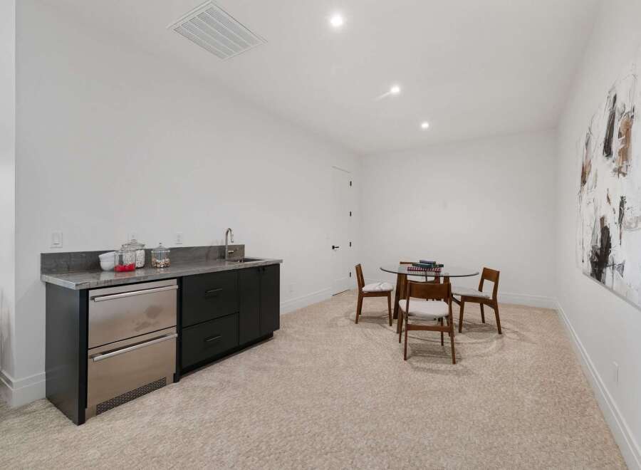 This spacious room features a modern wet bar with a stainless steel mini-fridge and ample cabinet space, perfect for entertaining.