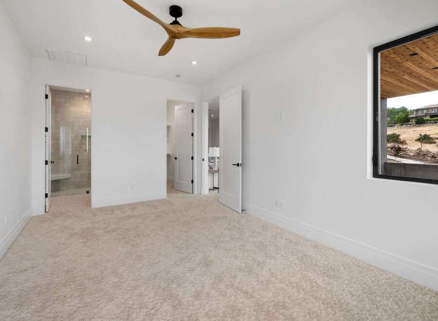 Experience modern luxury in this spacious bedroom featuring a sleek ceiling fan and plush carpeting.