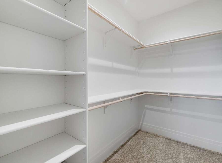 Discover ample storage in this spacious walk-in closet, featuring a built-in shelving unit on one side and multiple hanging rods on the other.