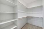 Discover ample storage in this spacious walk-in closet, featuring a built-in shelving unit on one side and multiple hanging rods on the other.