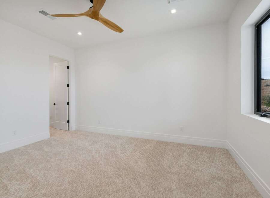 Experience modern living in this bright and airy bedroom, featuring plush carpeting and a sleek ceiling fan for optimal comfort.
