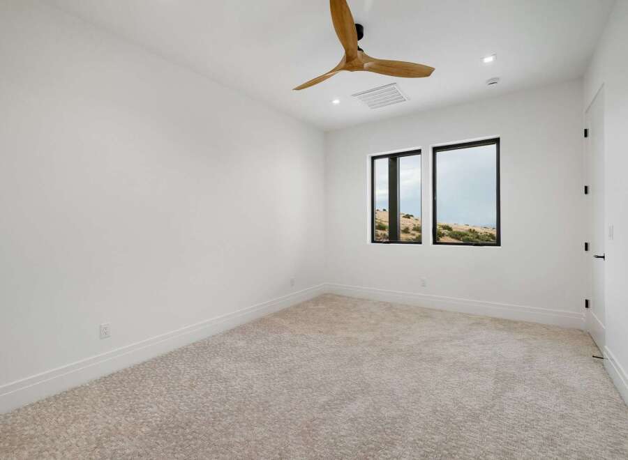 Experience modern living in this spacious bedroom featuring a sleek ceiling fan and large windows that offer stunning views of the natural landscape.