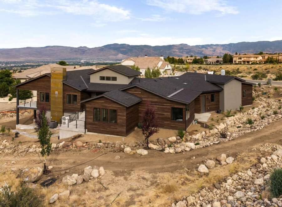 Discover this stunning modern home featuring rich wood siding and a striking metal chimney, set against a backdrop of rolling hills and distant mountains.