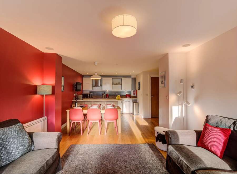Experience modern living in this open-plan apartment featuring a vibrant red accent wall and a fully equipped kitchen with sleek cabinetry.