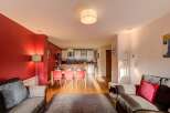 Experience modern living in this open-plan apartment featuring a vibrant red accent wall and a fully equipped kitchen with sleek cabinetry.