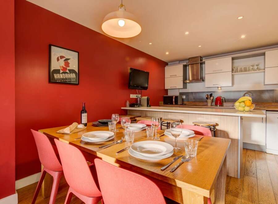 This inviting dining area features a warm red accent wall, a large wooden dining table set for a meal, and a modern kitchen with white cabinetry and stainless steel appliances.