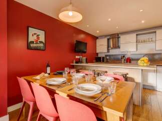 This inviting dining area features a warm red accent wall, a large wooden dining table set for a meal, and a modern kitchen with white cabinetry and stainless steel appliances.