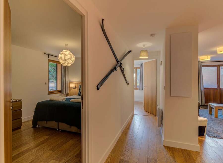 Step into this charming hallway featuring a unique ski decor, leading to a cozy bedroom with a modern pendant light and a window overlooking greenery.