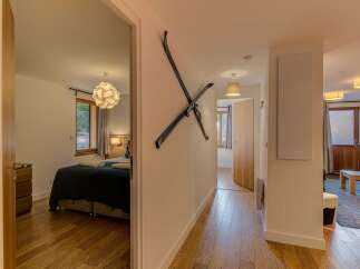 Step into this charming hallway featuring a unique ski decor, leading to a cozy bedroom with a modern pendant light and a window overlooking greenery.