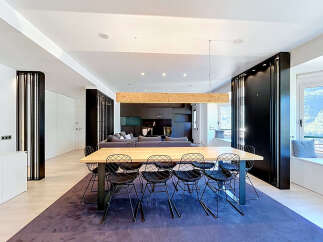 Experience modern living in this spacious open-concept dining and living area, featuring a striking wooden beam chandelier above a large dining table with contemporary wire chairs.