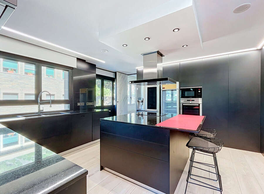 Experience modern luxury in this sleek, black kitchen featuring a spacious island with a vibrant red countertop, perfect for entertaining.