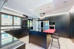 Experience modern luxury in this sleek, black kitchen featuring a spacious island with a vibrant red countertop, perfect for entertaining.