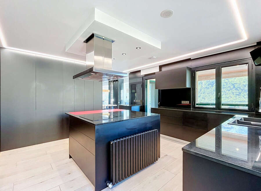 Experience modern luxury in this sleek, contemporary kitchen featuring a striking island with a built-in cooktop and vibrant red accent.