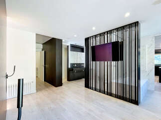 Experience modern luxury in this open-concept living space, featuring a sleek black slatted room divider with an integrated TV.
