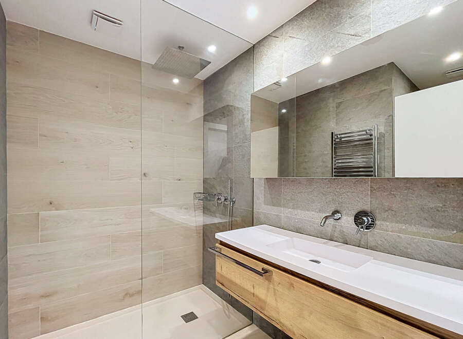 Experience modern luxury in this stunning bathroom featuring a spacious walk-in shower with a rainfall showerhead and elegant wood-look tiles.