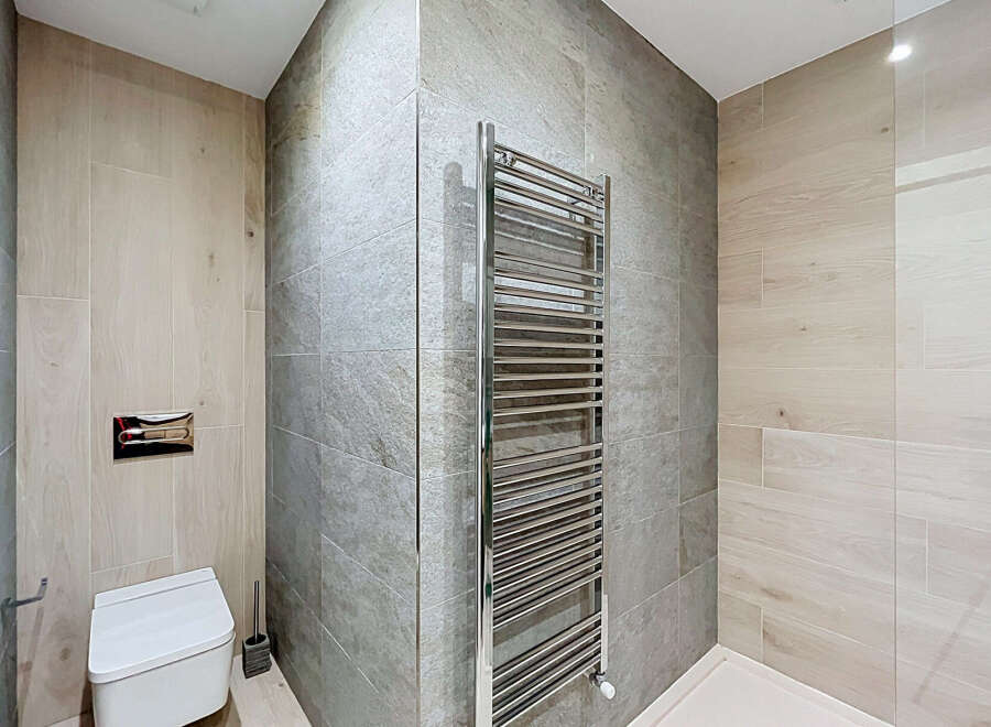This modern bathroom features a sleek, wall-mounted toilet with a chrome flush plate, complemented by a stylish chrome towel warmer.