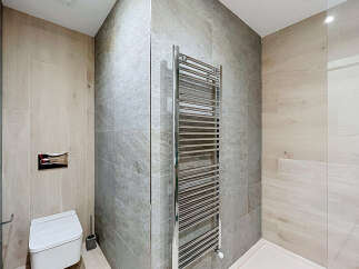 This modern bathroom features a sleek, wall-mounted toilet with a chrome flush plate, complemented by a stylish chrome towel warmer.