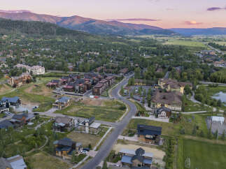 Discover luxury mountain living in this stunning aerial view of a modern residential development nestled amidst rolling hills and majestic peaks.