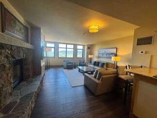Experience luxury living with this stunning mountain view condo, featuring a cozy stone fireplace and a spacious living area perfect for relaxation.