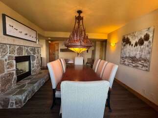 Experience rustic elegance in this dining room, featuring a grand stone fireplace and a unique tree-themed chandelier.