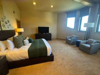 Experience ultimate comfort in this spacious bedroom, featuring a luxurious king-size bed adorned with plush pillows and a rich green accent throw.