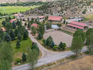 Discover this expansive ranch property, featuring multiple buildings with red roofs, including barns and residential structures, set against a backdrop of rolling hills and lush greenery.