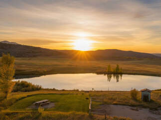 Experience the serene beauty of this property at sunset, featuring a tranquil pond reflecting the golden sky.