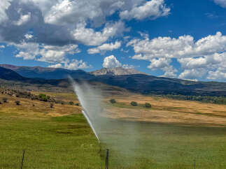Experience the beauty of this expansive rural property, featuring lush green fields being irrigated by a sprinkler system.