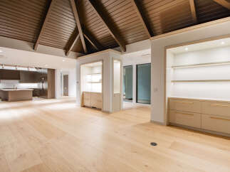 Experience modern luxury in this open-concept living space featuring a stunning vaulted wood-paneled ceiling and sleek, built-in cabinetry with integrated lighting.
