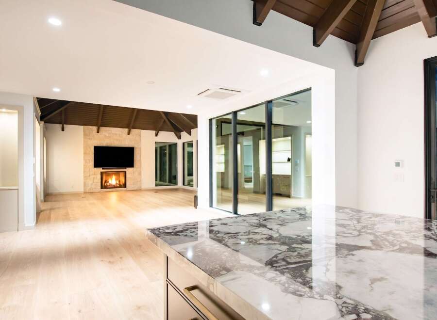 Experience modern luxury in this stunning open-concept living space, featuring a captivating stone fireplace and expansive glass doors that seamlessly blend indoor and outdoor living.