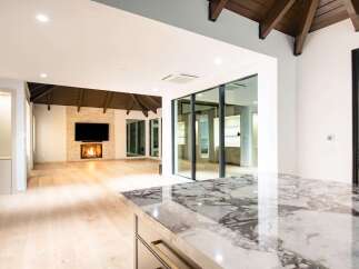 Experience modern luxury in this stunning open-concept living space, featuring a captivating stone fireplace and expansive glass doors that seamlessly blend indoor and outdoor living.