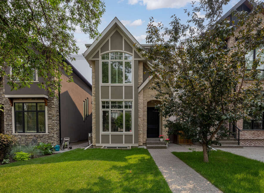 This charming home features a striking facade with a mix of stone and stucco finishes, complemented by a large arched window on the upper level.
