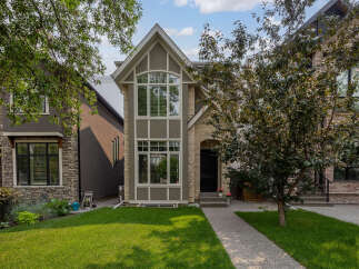 This charming home features a striking facade with a mix of stone and stucco finishes, complemented by a large arched window on the upper level.