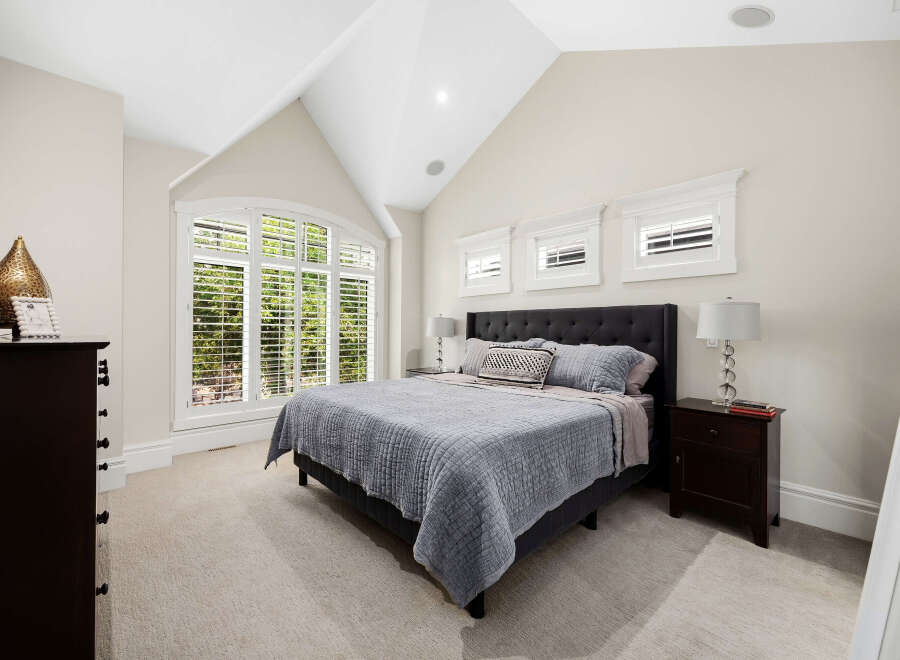 Experience luxury in this master bedroom, featuring a grand arched window with plantation shutters that flood the space with natural light.