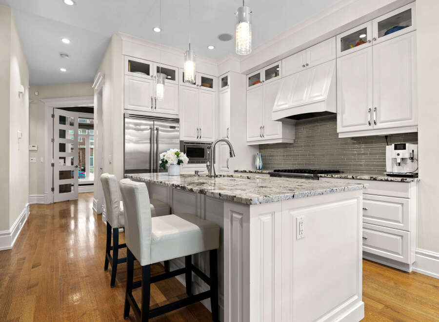 Experience luxury in this stunning kitchen featuring sleek white cabinetry, a spacious granite island with bar seating, and high-end stainless steel appliances.