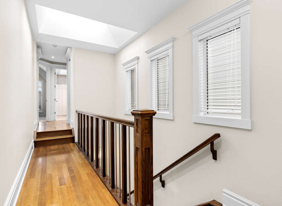 This spacious hallway features a beautiful wooden staircase with a dark wood banister and white spindles, leading to a bright upper level.