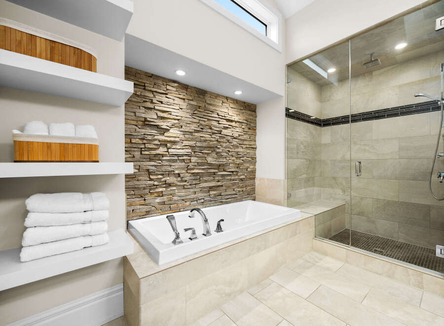 Experience luxury in this stunning bathroom featuring a deep soaking tub set against a captivating stacked stone accent wall.