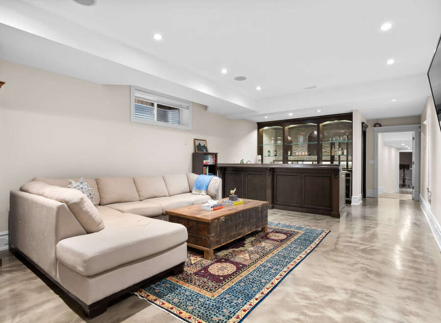 This finished basement offers a stylish entertainment space with a large sectional sofa, a rustic wooden coffee table, and a built-in bar with glass-front cabinets perfect for showcasing beverages.