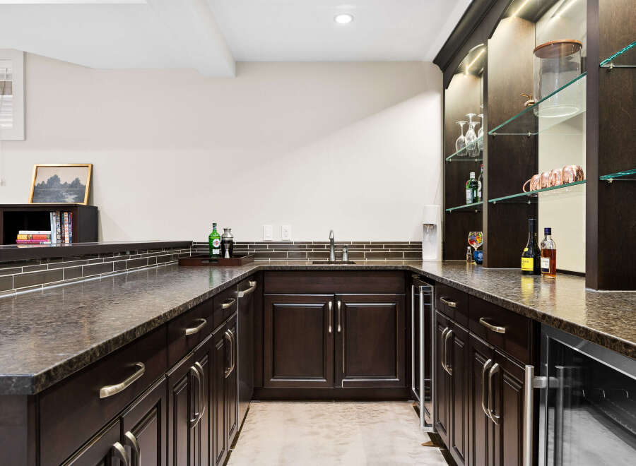 This elegant home bar features dark wood cabinetry with brushed nickel hardware, complemented by a speckled granite countertop.