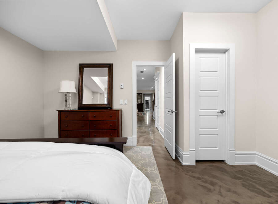 This bedroom offers a serene retreat with its neutral color palette and elegant dark wood dresser topped with a decorative mirror and lamp.